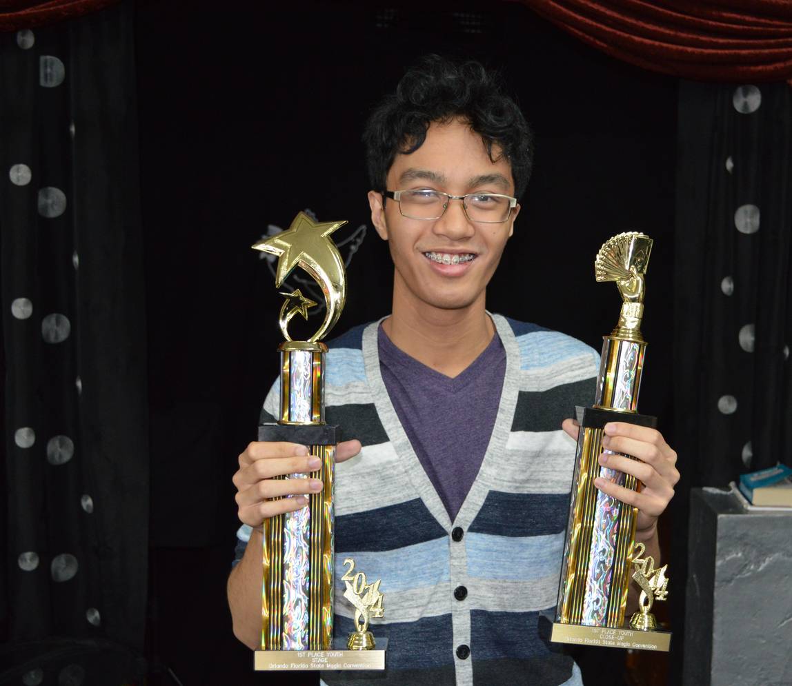 A boy with braces holding two trophies