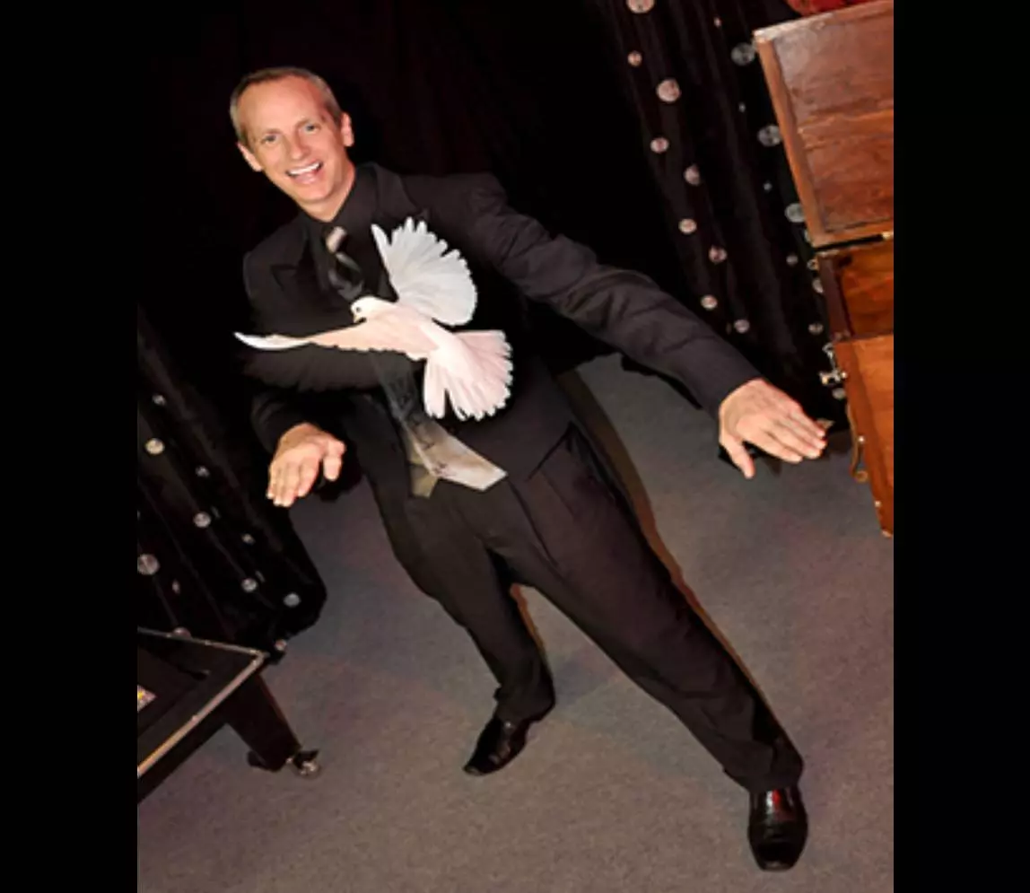 A magician wearing a black color suit and smiling