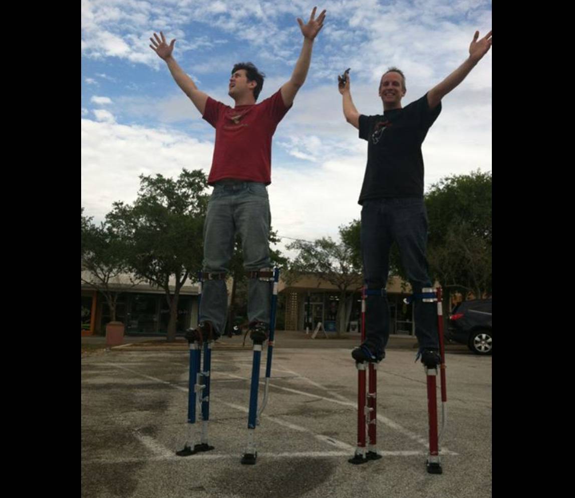 Two men with long prosthetics and raising their hand