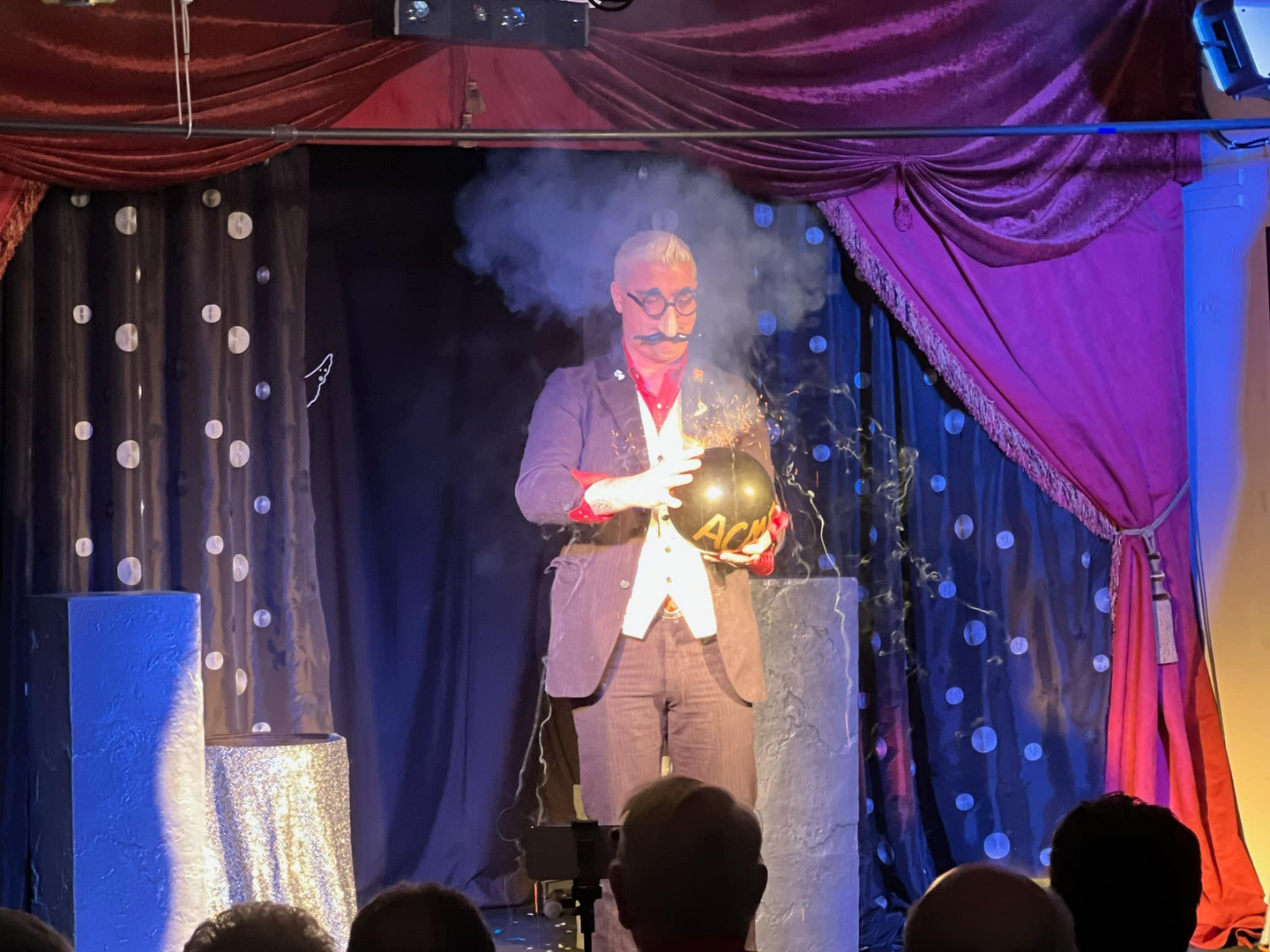 A man in a suit standing on stage with smoke coming out of his mouth.