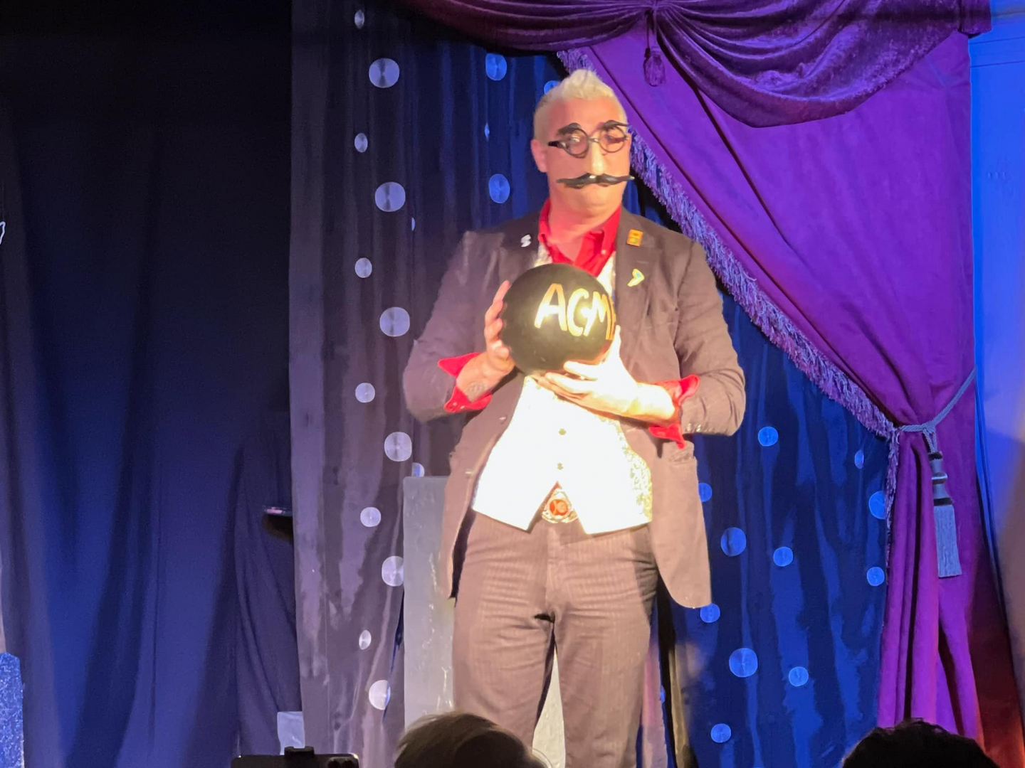 A man in a suit holding a ball on stage.