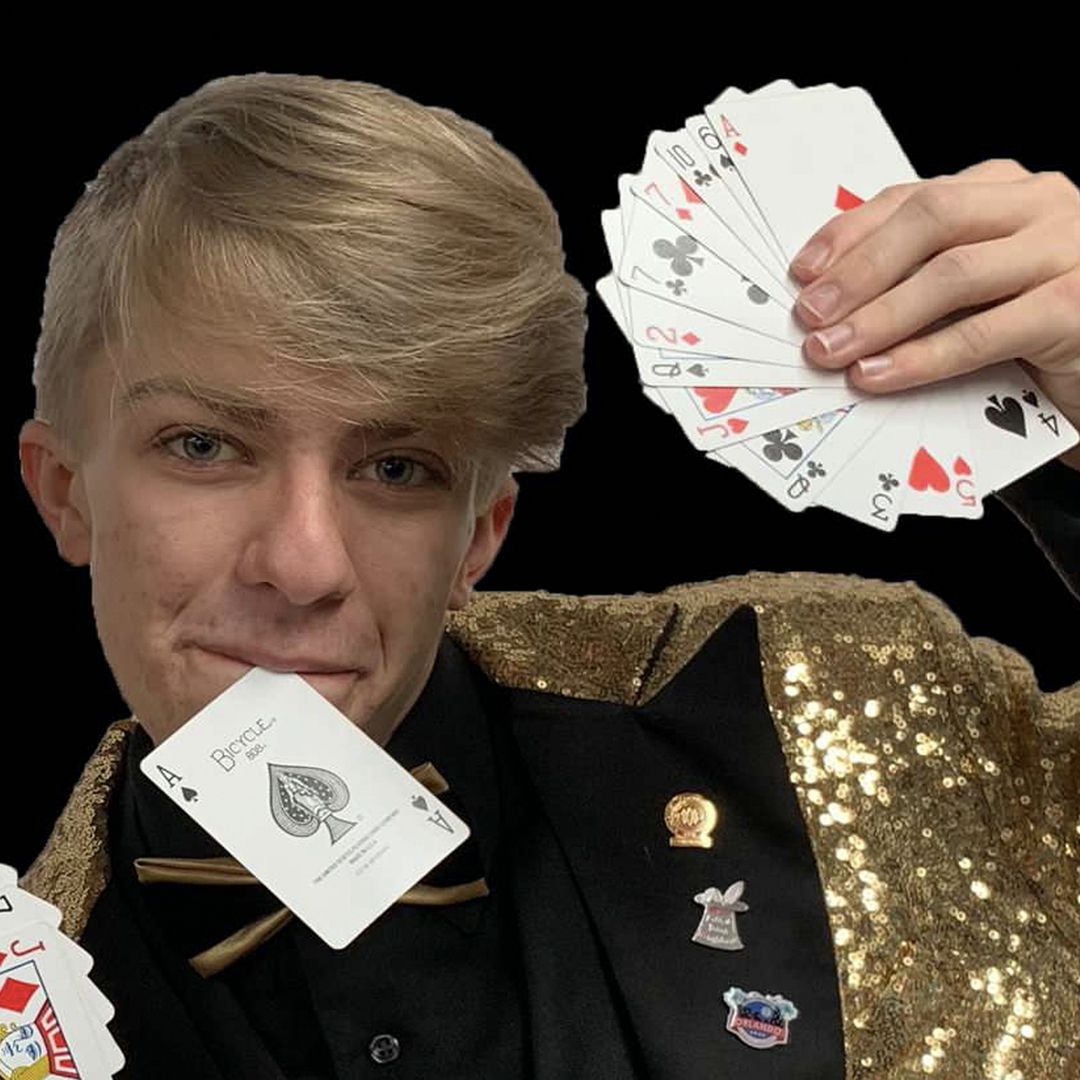 A young man in a tuxedo holding up playing cards.