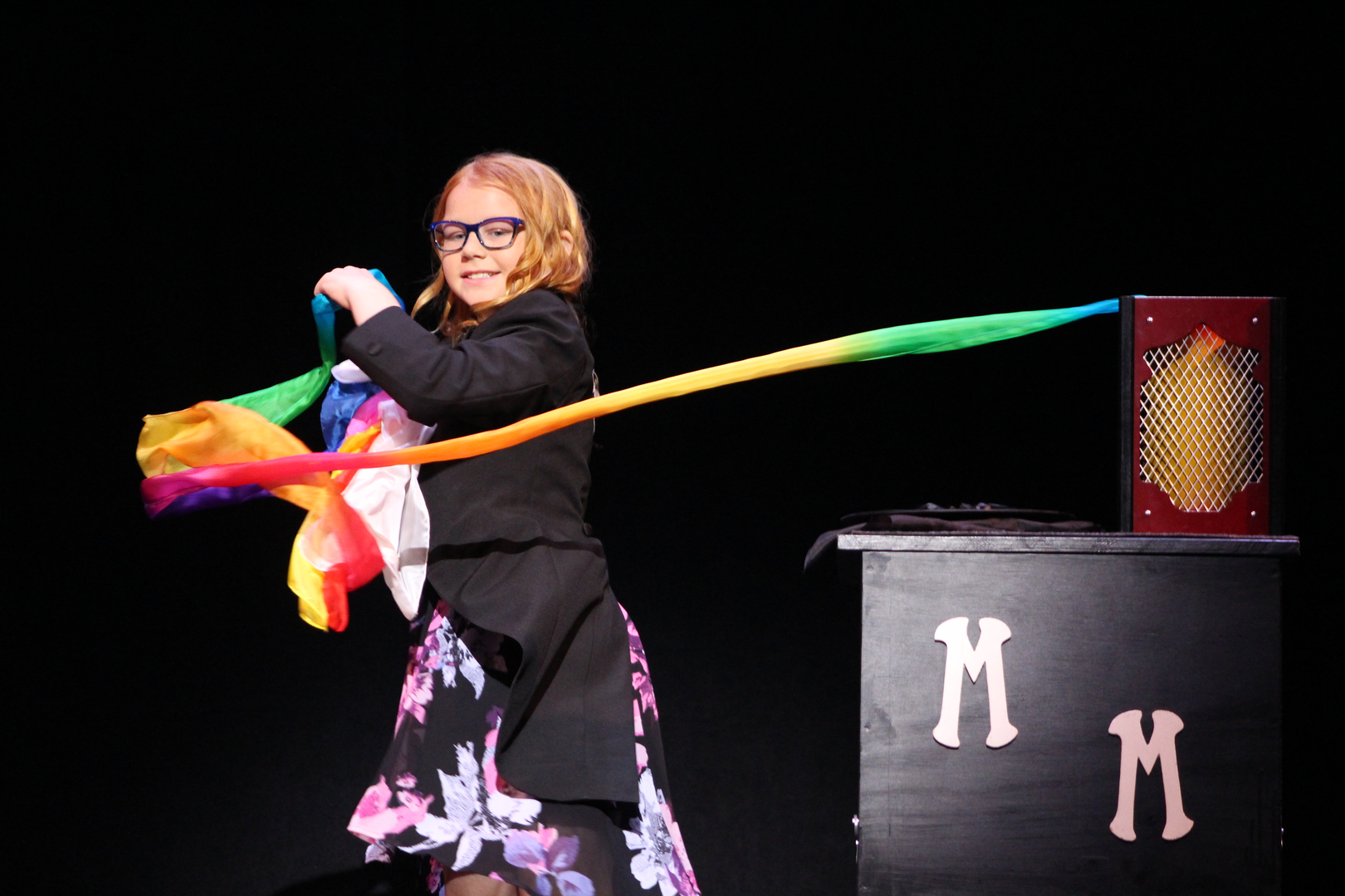 A woman holding a rainbow ribbon on stage.