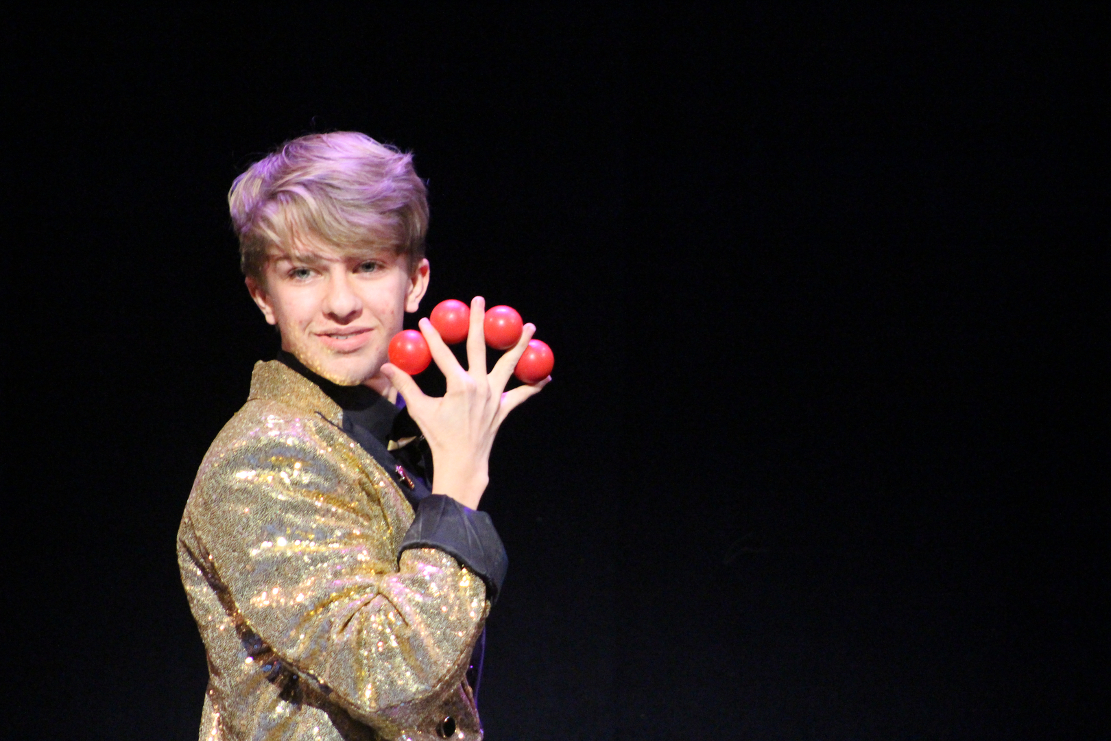 A young man in a gold suit holding two red apples.