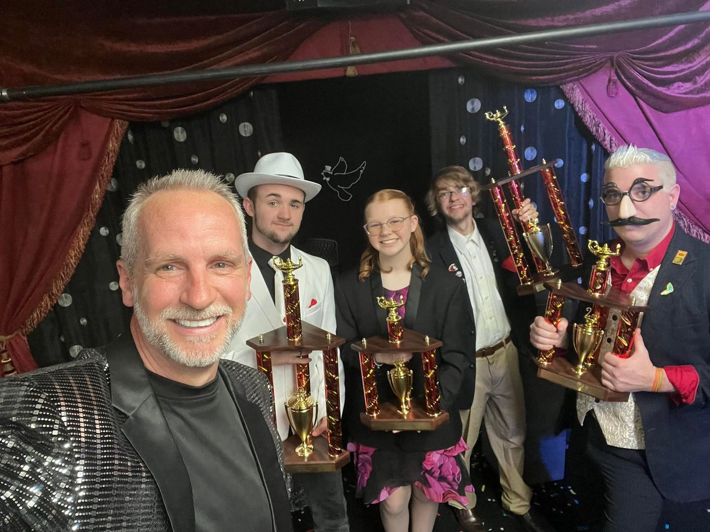 A group of people holding trophies in front of a stage.
