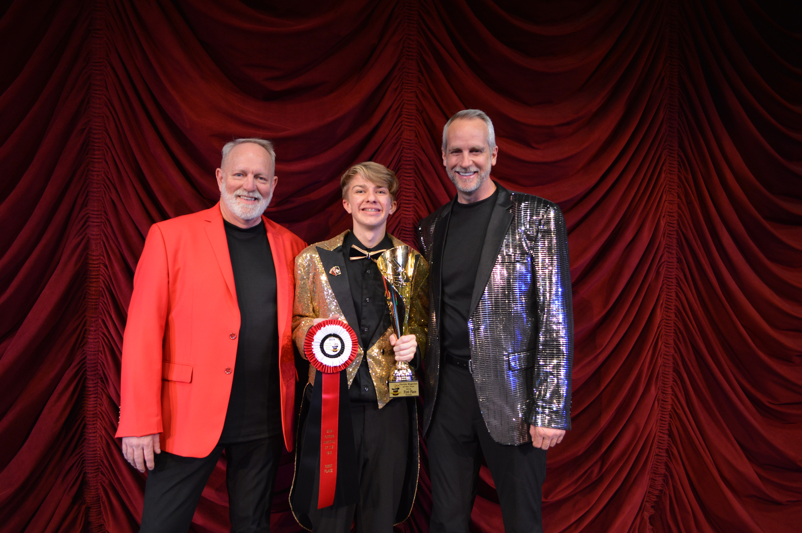 Three people posing for a picture in front of a red curtain.
