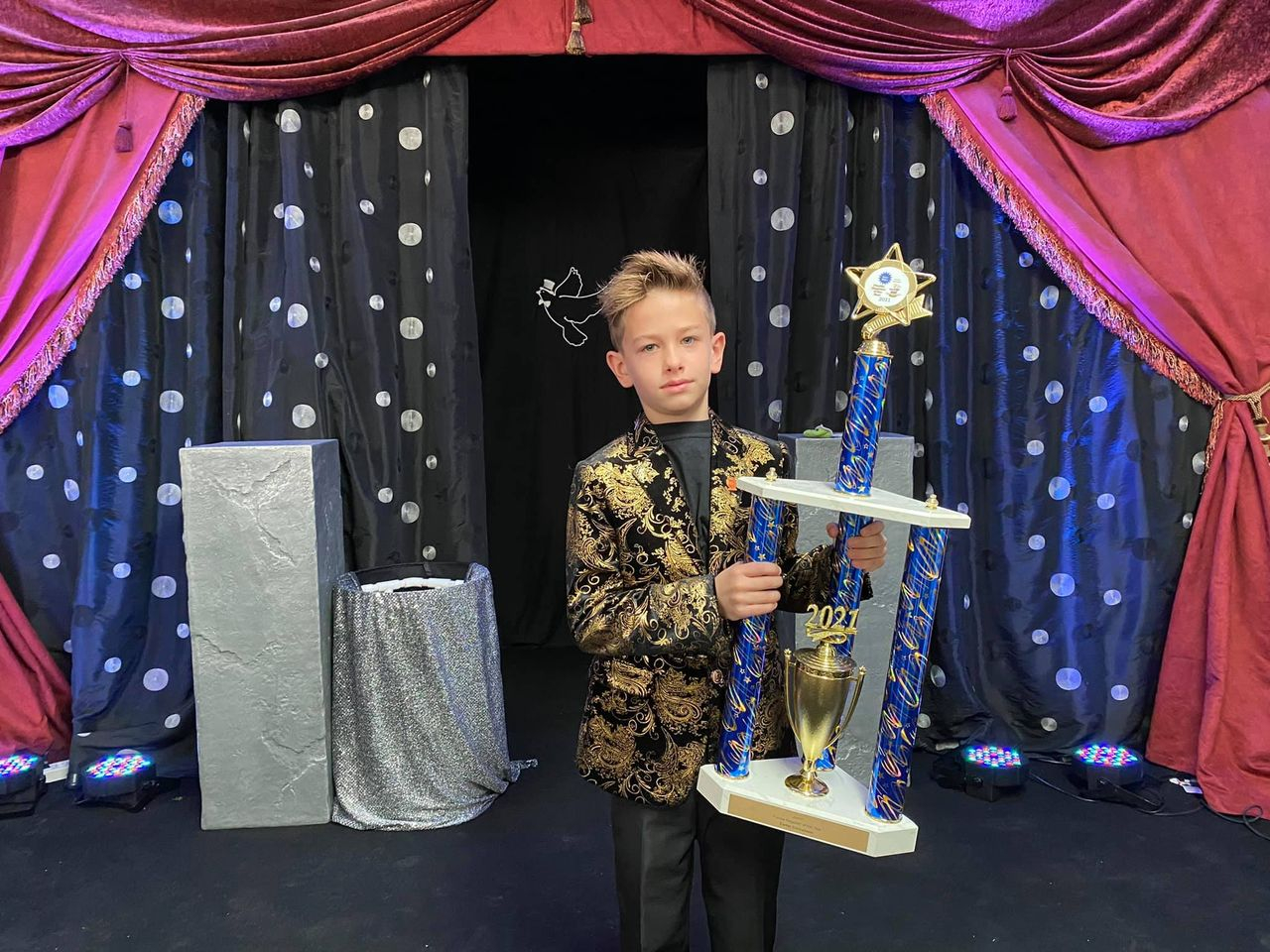 A young boy holding a trophy in front of a stage.