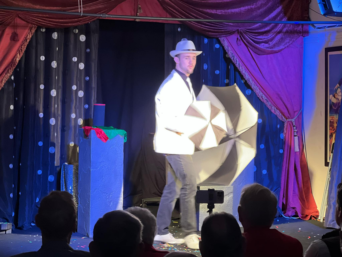 A man in a hat is holding an umbrella in front of an audience.