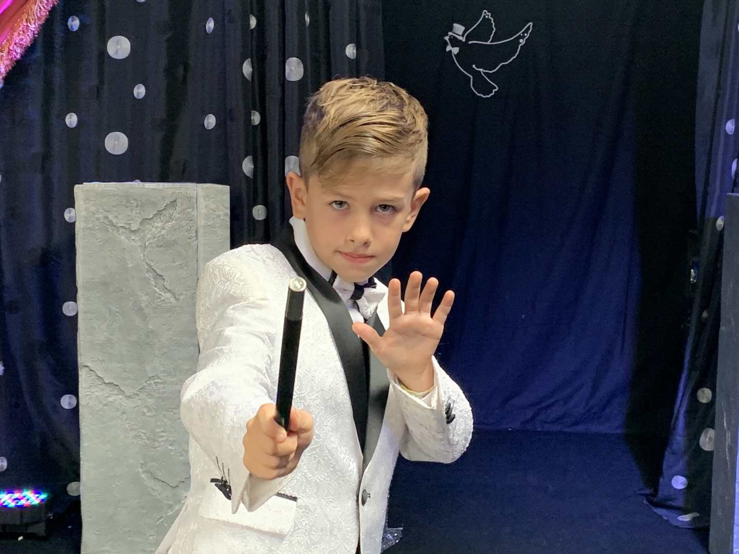 A young boy in a tuxedo holding a magic wand.